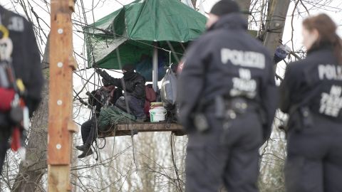 In the background you can see a platform that activists have erected between trees. There are several activists on the platform. In the foreground, police officers can be seen in a blur from behind.