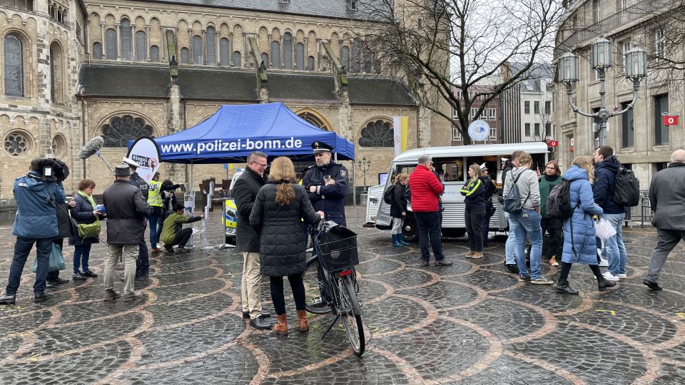 Der Infostand der Bonner Polizei mit vielen Menschen sowie einer Radfahrerin im Vordergrund