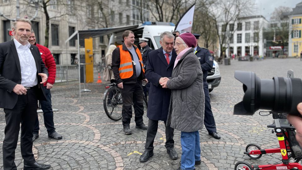 Eine Menschengruppe vor dem Infostand der Polizei, Innenminister Herbert Reul unterhält sich mit einer älteren Dame