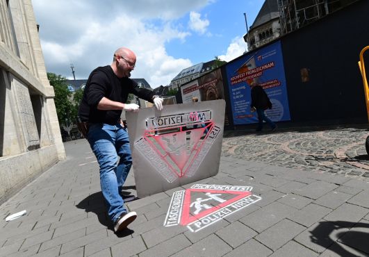 Ein Polizist zeigt die Schablone, mit der die Symbole zur Warnung vor Taschendieben auf die Straße gesprüht werden